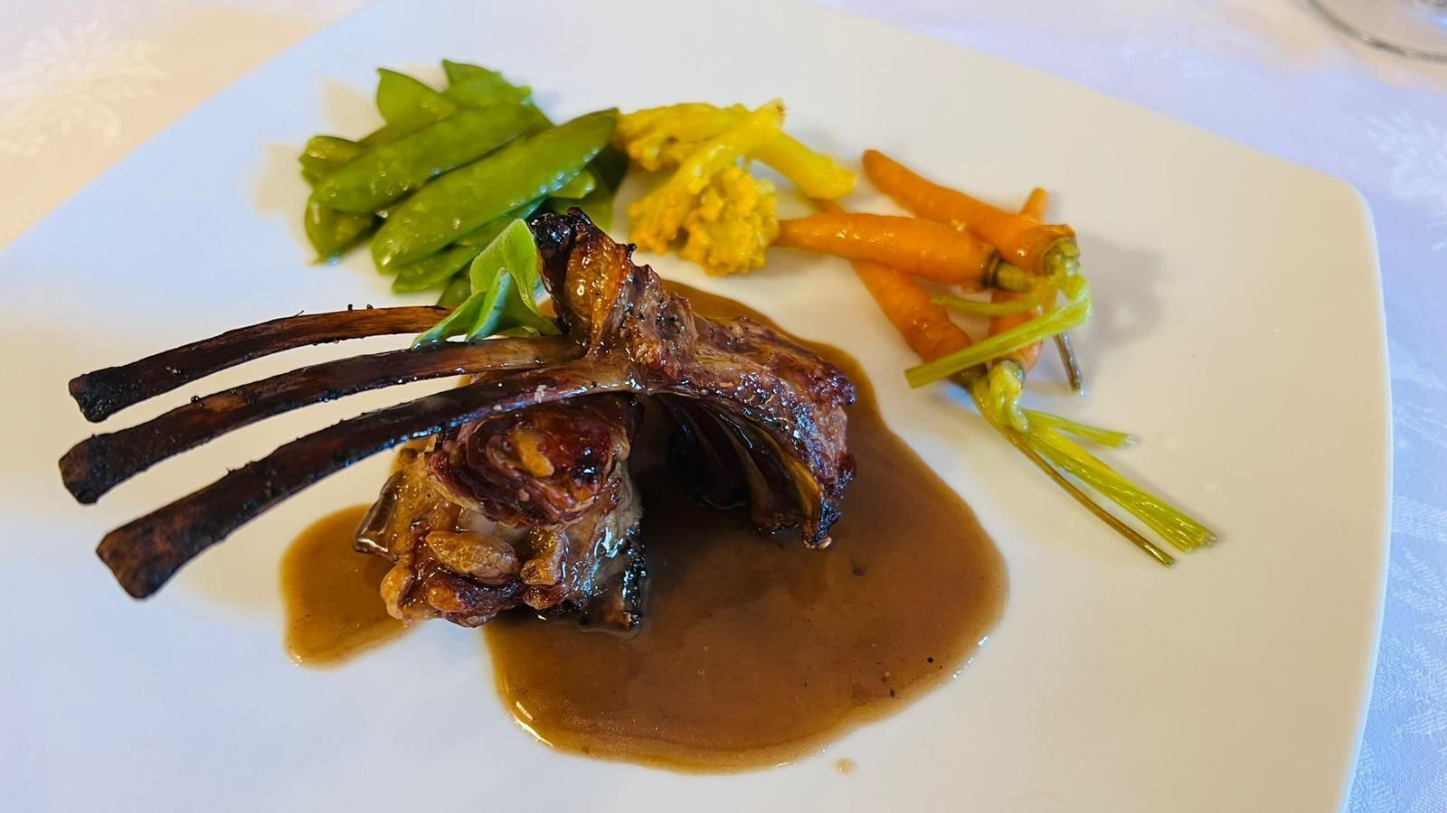Un plato con una costilla de cordero, judías verdes, zanahorias y un guarnición de verdura amarilla.