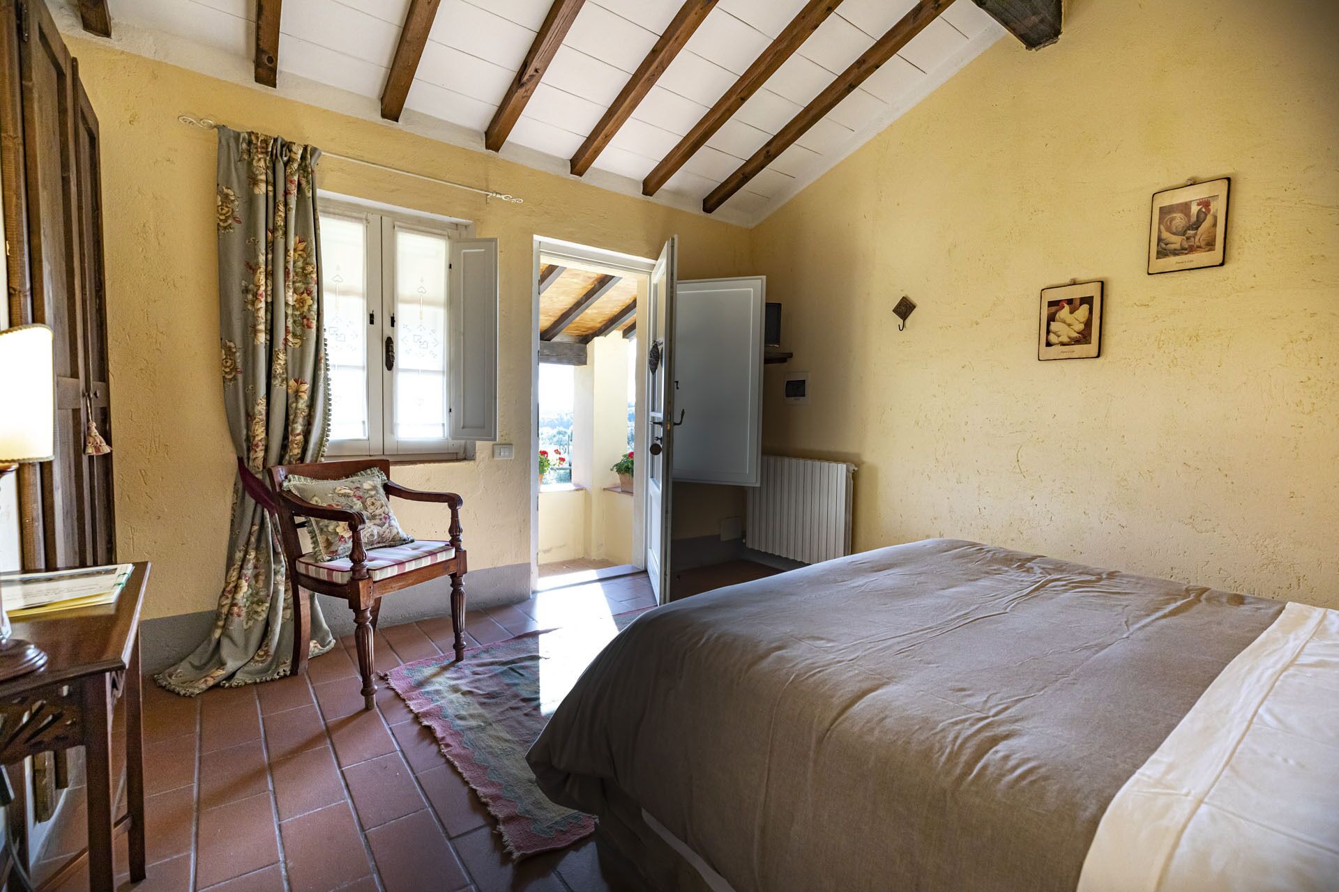 A bedroom with a bed, a chair, a table, a window with curtains, and a door leading outside.