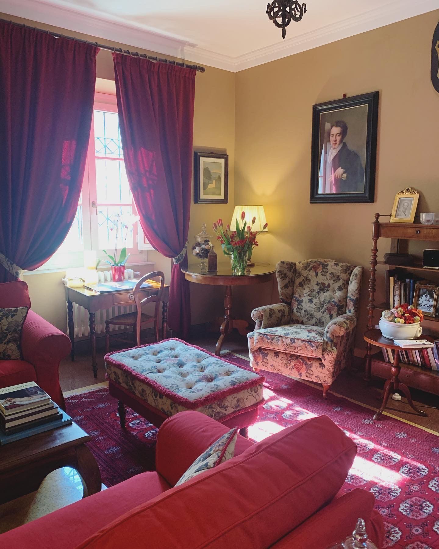 A traditional living room with red sofas, a floral armchair, a wooden side table, and a lamp.