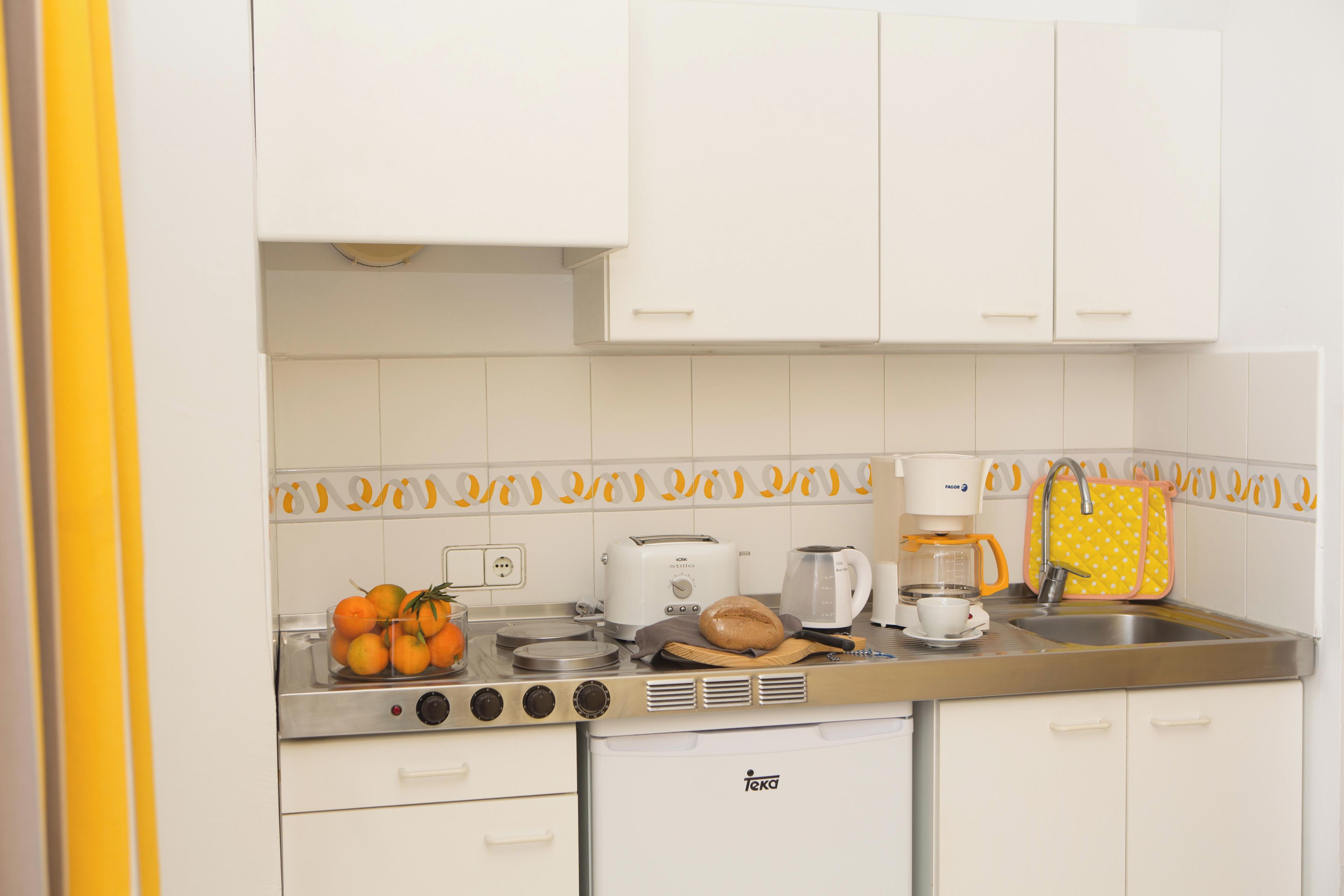 Una kitchenette funcional con estufa, tostadora, cafetera y un refrigerador pequeño.
