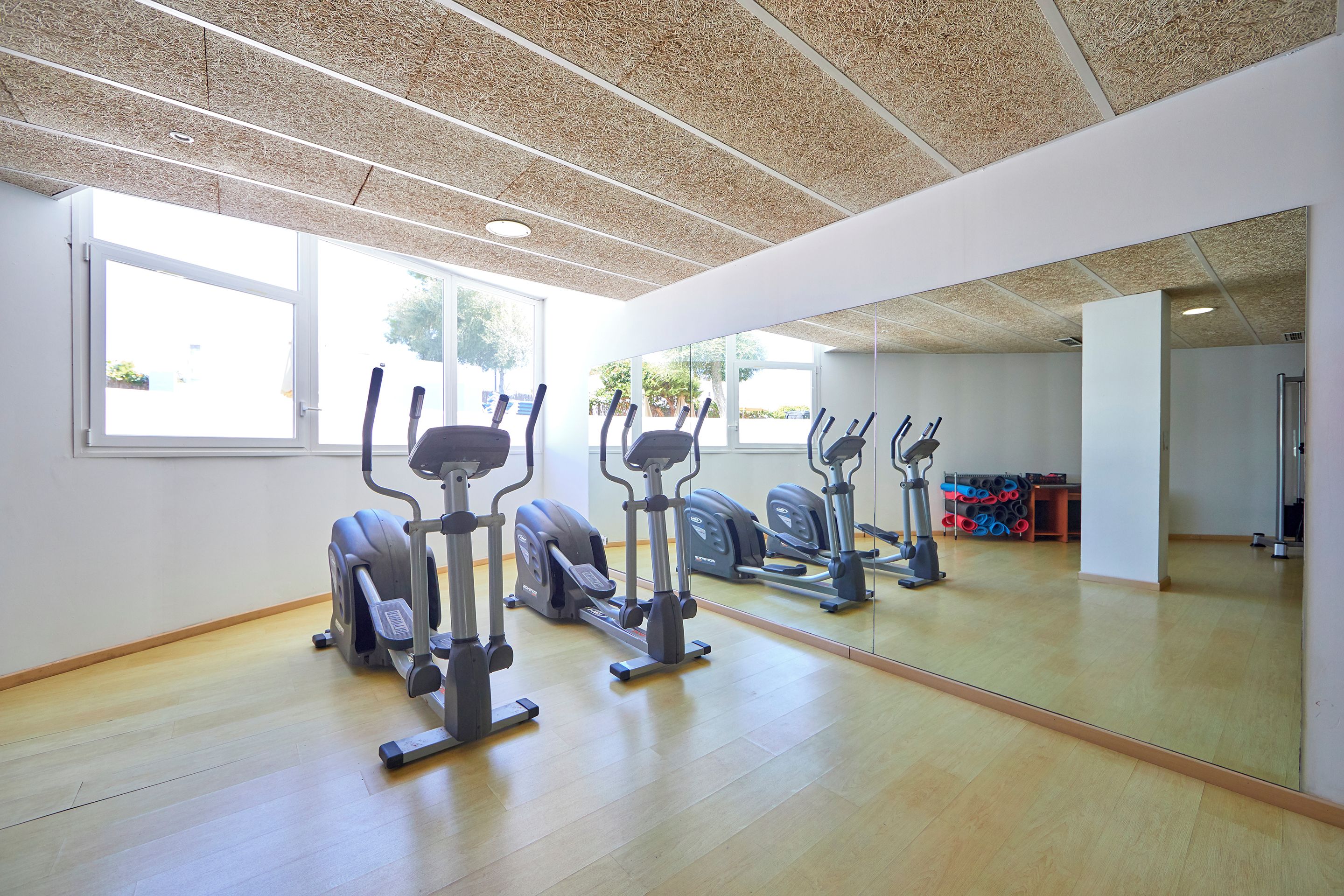 A gym with exercise equipment, large windows, and a wooden floor.