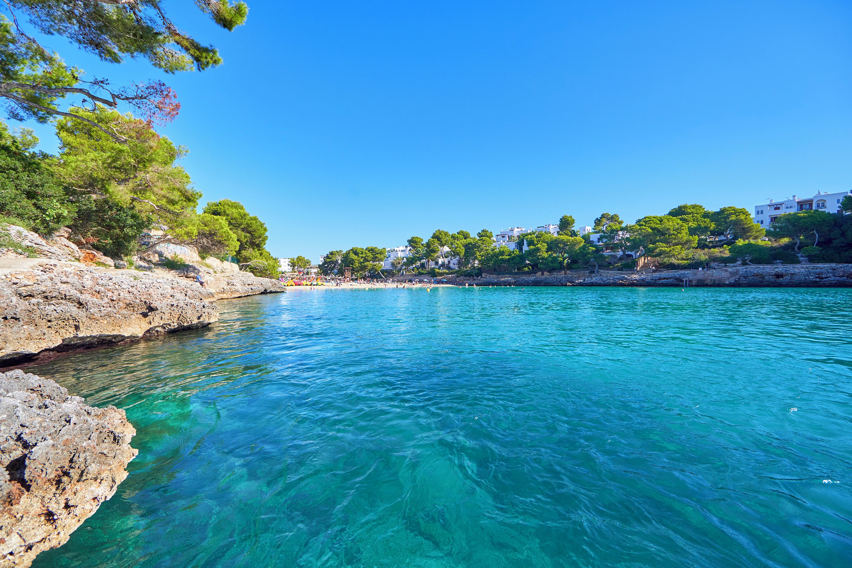 Eine Küstenlandschaft mit klarem türkisblauem Wasser, felsigen Ufern und Gebäuden im Hintergrund.
