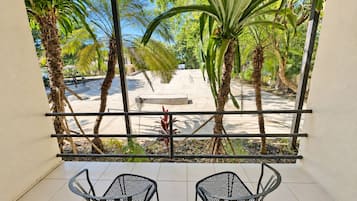 Een balkon met twee stoelen, uitzicht op een zandrijk gebied met palmbomen, en een bank.