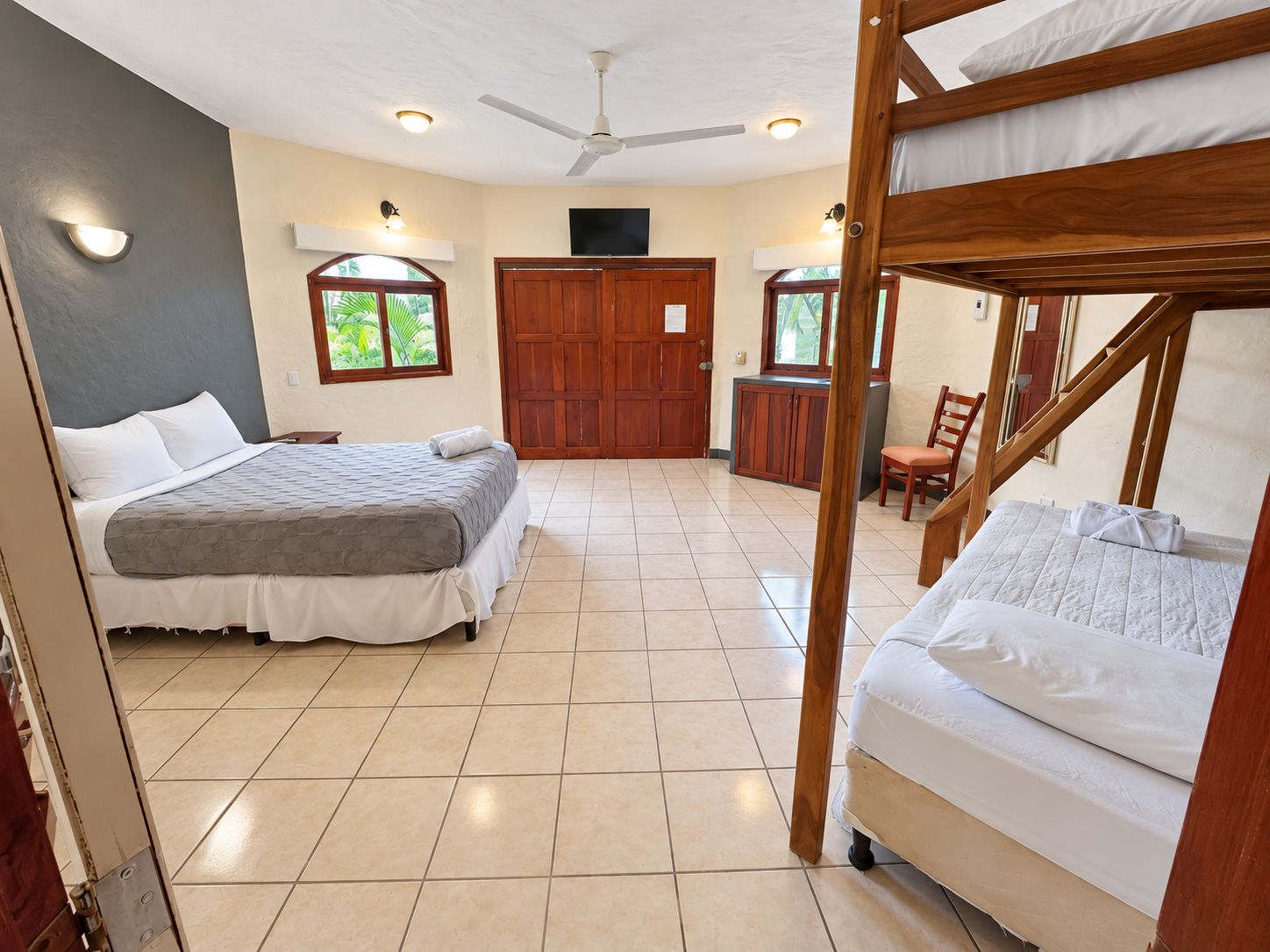 A room with two beds, a ceiling fan, a wooden door, and a small table.
