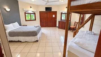 A room with two beds, a ceiling fan, a wooden door, and a small table.