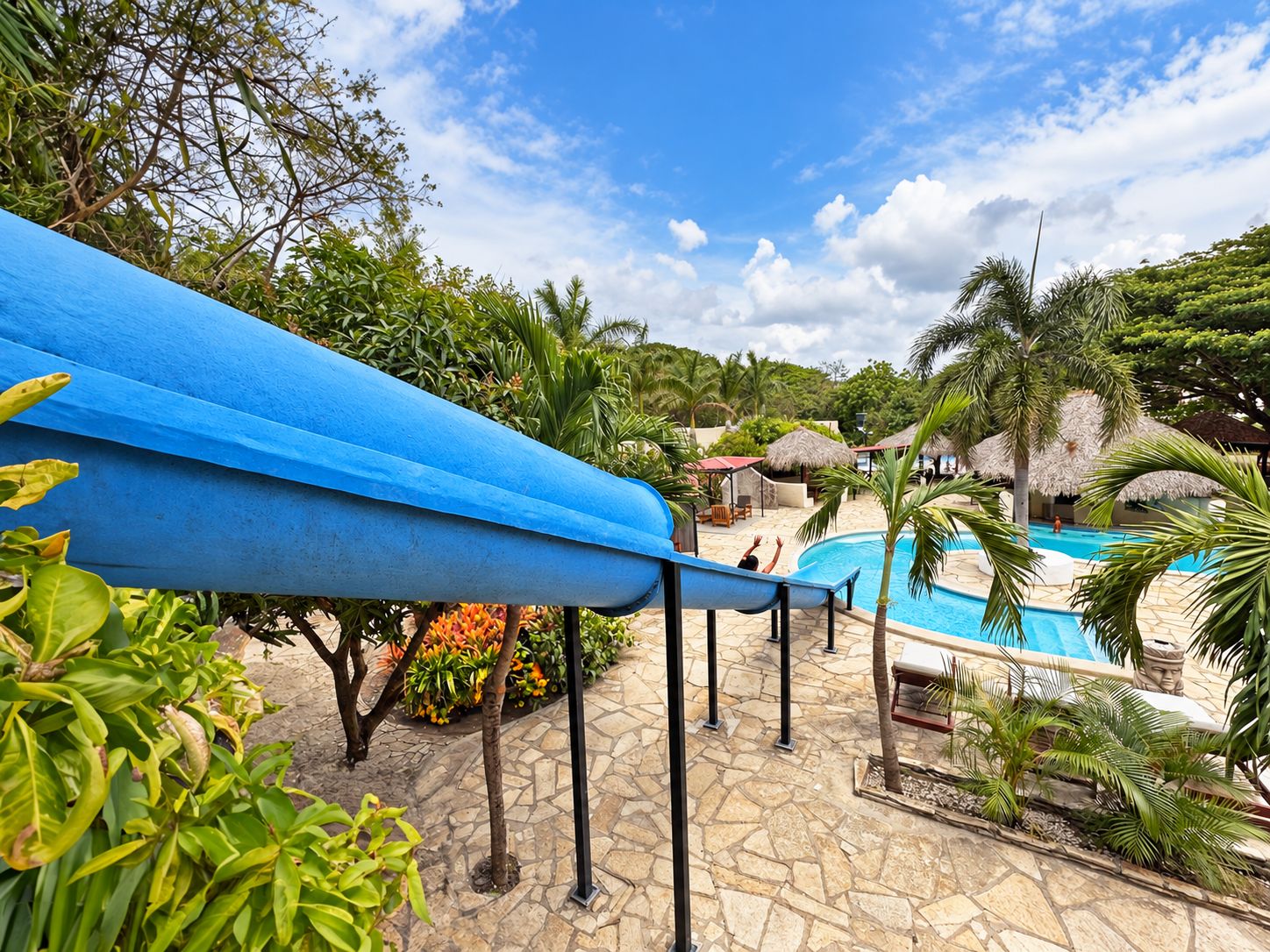 A pool area with a blue canopy, palm trees, and a stone pathway.