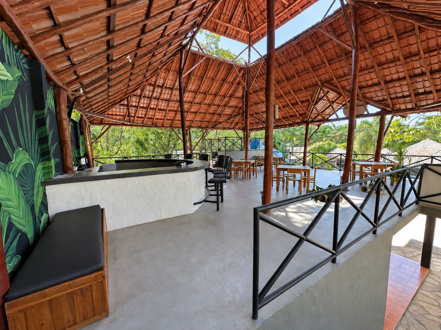 Un espace extérieur aménagé avec un toit de chaume, un comptoir de bar, des tables et des chaises.