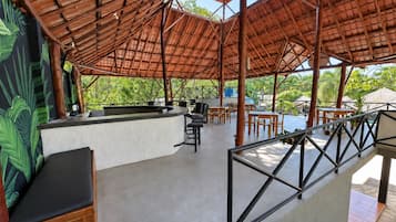 Un espace extérieur aménagé avec un toit de chaume, un comptoir de bar, des tables et des chaises.