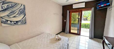 Une chambre d’hôtel équipée d’un lit, d’un ventilateur de plafond, d’un appareil de climatisation, d’une télévision et d’une porte-fenêtre coulissante donnant sur un balcon.