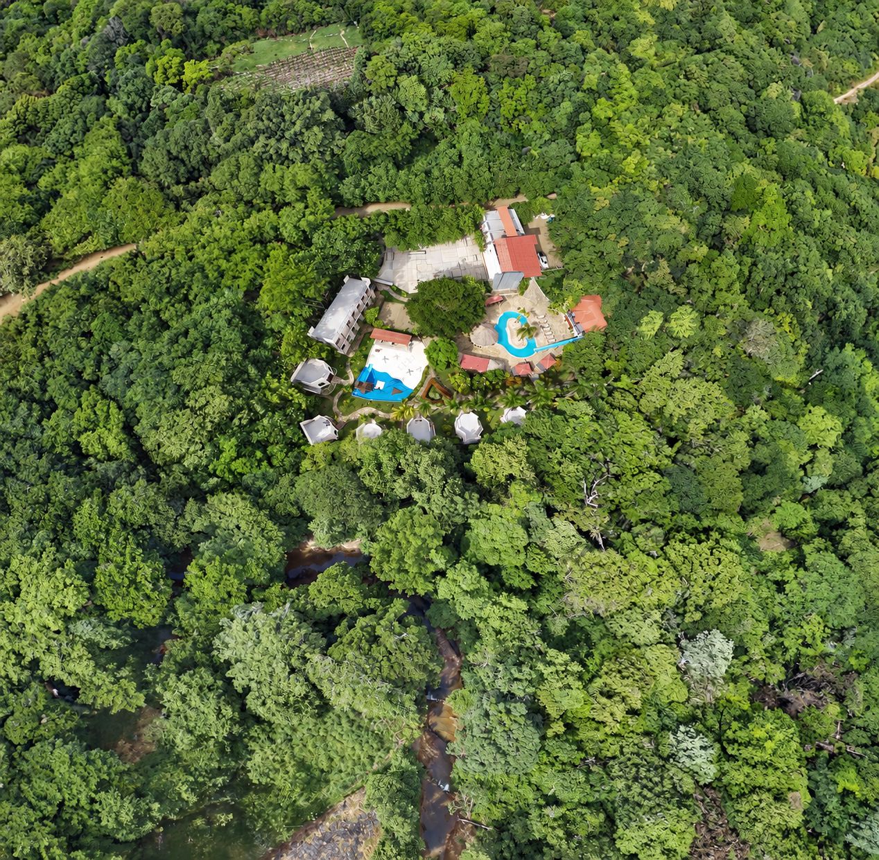 Vista aérea de una propiedad con piscina, varias edificaciones y abundante vegetación circundante.
