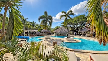 A resort pool area with multiple pools, lounge chairs, and palm trees.