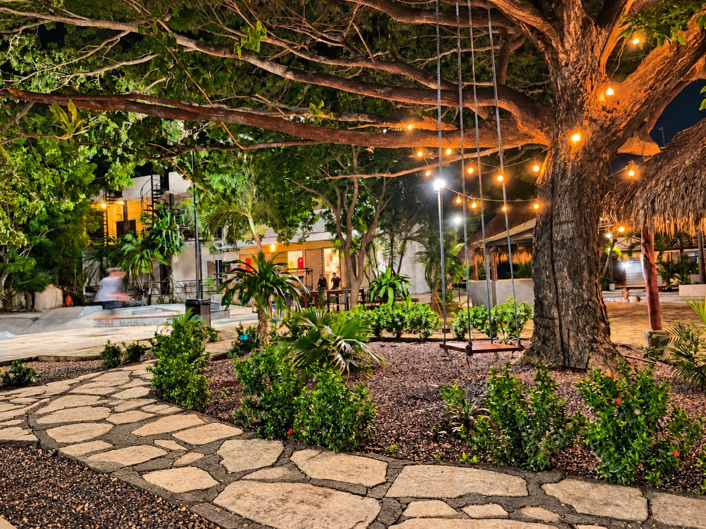An outdoor area with stone pathways, a large tree, and string lights.