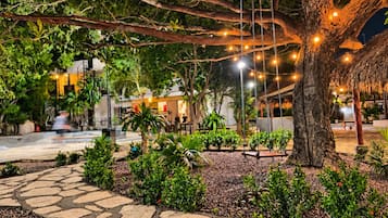 An outdoor area with stone pathways, a large tree, and string lights.
