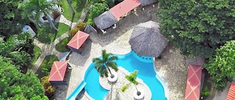 Vista aérea de un complejo turístico con varias piscinas, palmeras y estructuras de techo de paja.