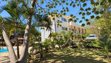 A hotel with a swimming pool, surrounded by palm trees and a well-maintained lawn.