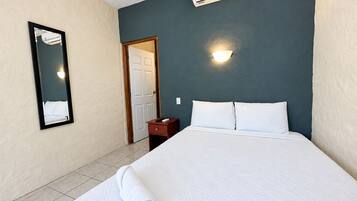 A hotel room with a bed, a nightstand, a mirror, a door, and an air conditioning unit.