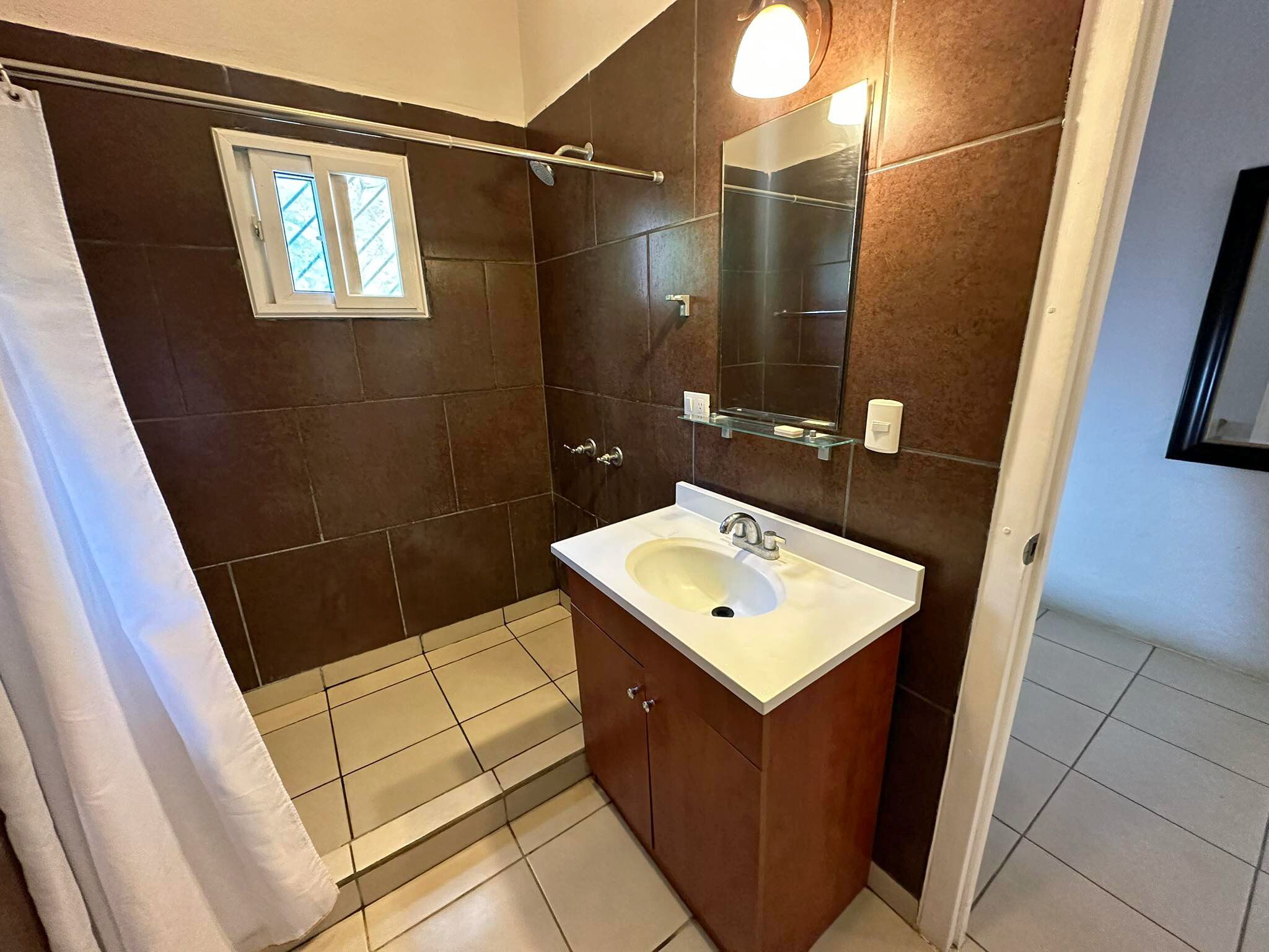 Un baño con ducha, lavamanos y espejo.