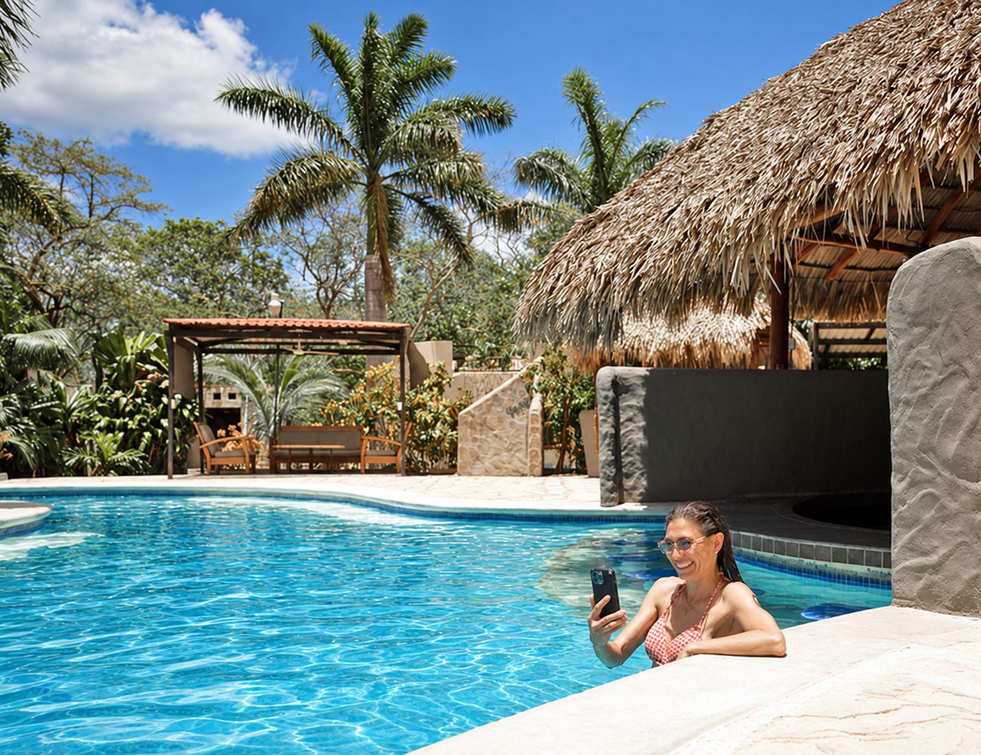 A swimming pool with a thatched-roof structure, lounge chairs, and palm trees.