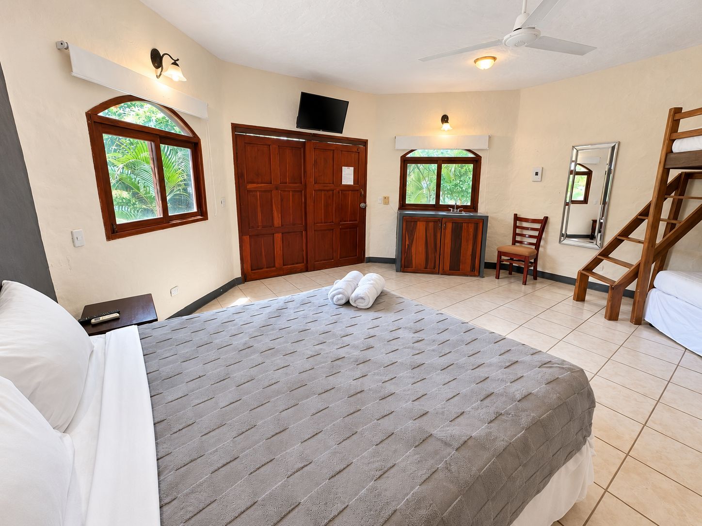 A hotel room with a bed, a desk, a chair, a wardrobe, a TV, and a window with a view of greenery.