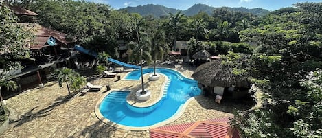 A pool area with a central circular pool, lounge chairs, and a thatched-roof structure.