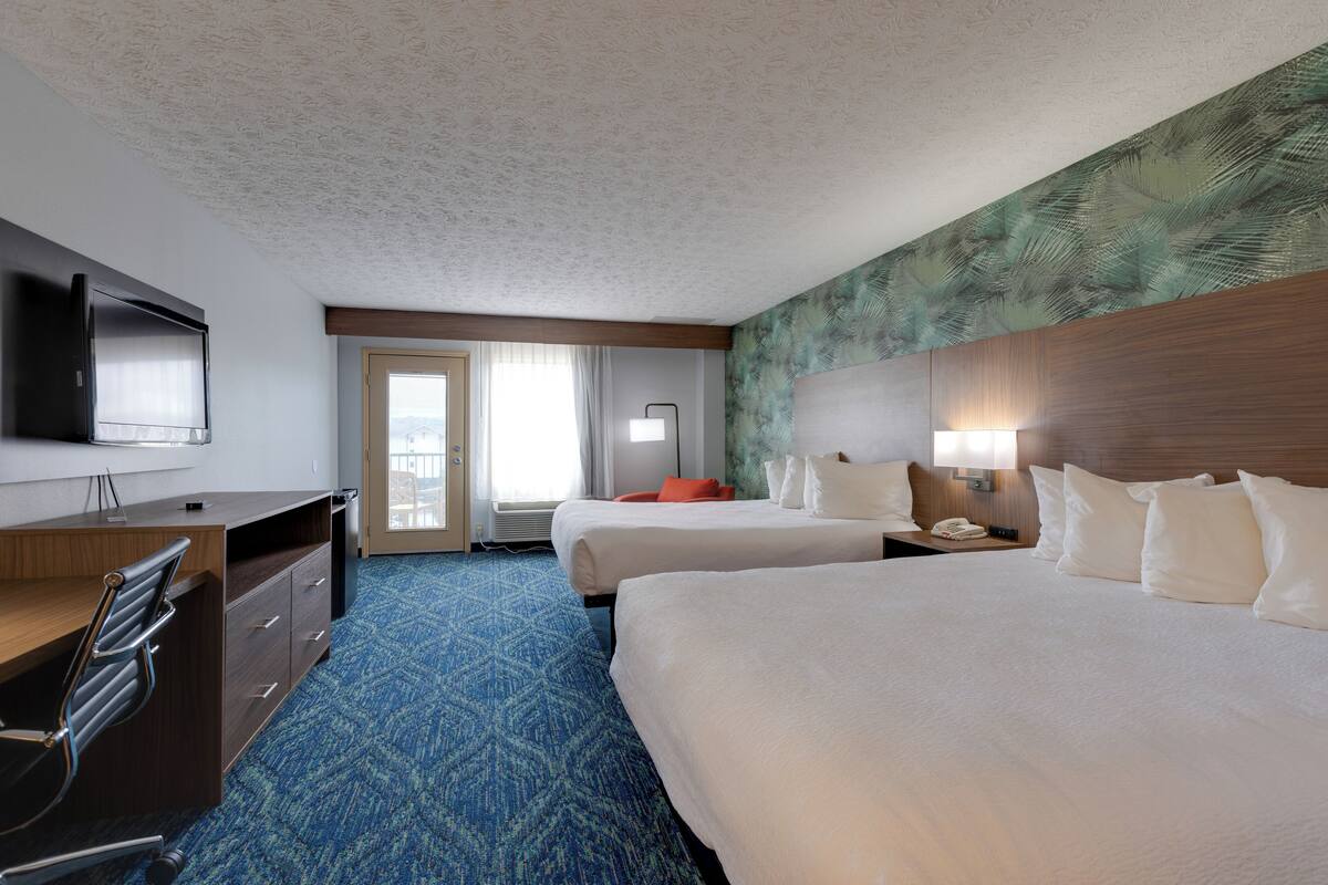 A hotel room with two beds, a desk, a chair, a television, and a window with curtains.