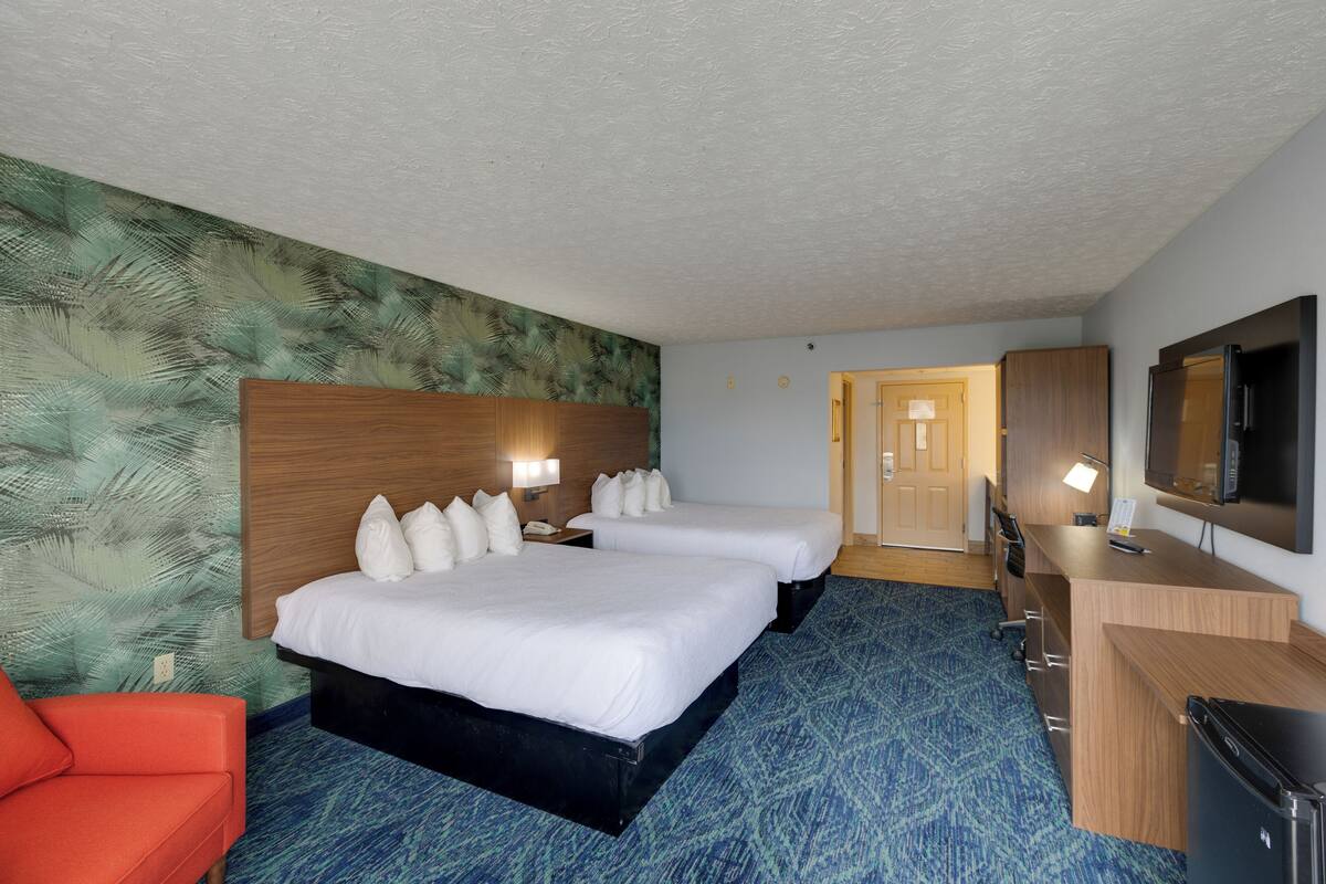 A hotel room with two beds, a desk, a TV, and a red chair.