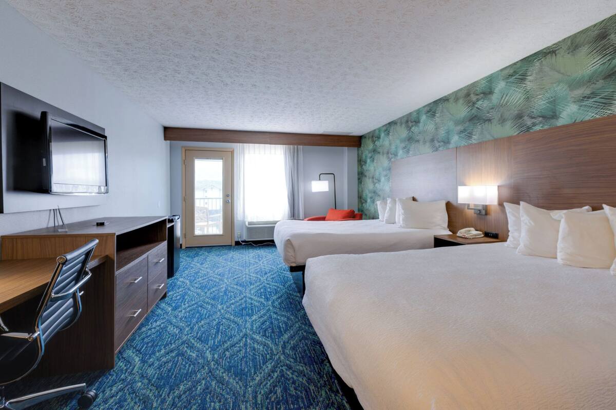 A hotel room with two beds, a desk, a chair, a television, and a door leading to a balcony.