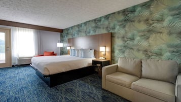 Habitación de hotel con una cama grande, un sofá, una mesita de noche con lámpara y una pared con diseño de hojas.