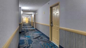 A hotel hallway with patterned carpet, cream walls, and doors with a gold handle.