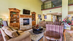 A spacious living room with a stone fireplace, comfortable seating, a flat-screen TV, and a balcony with decorative railings. - Park Grove Inn (Pigeon Forge)
