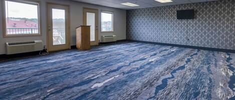 Un salón de conferencias con alfombra estampada, ventanas amplias y una televisión montada.