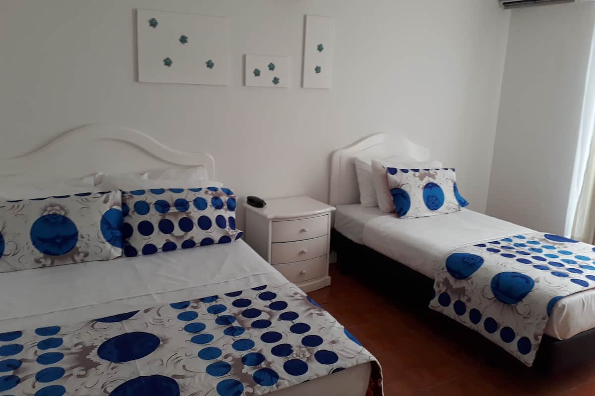 Une chambre à coucher avec deux lits, chacun agrémenté de draps bleus et blancs, une table de chevet blanche et des œuvres d’art accrochées au mur.