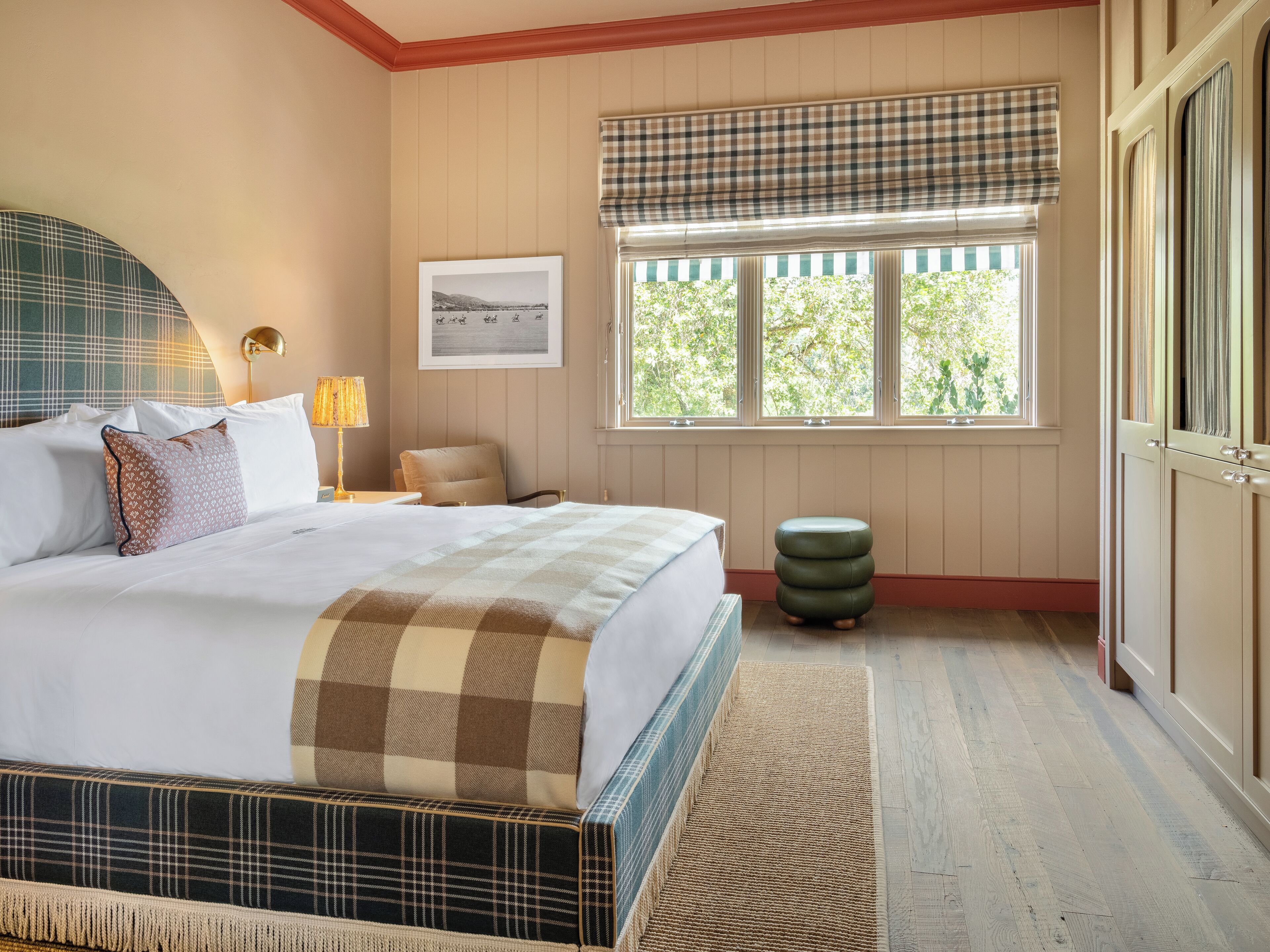 A neatly arranged bedroom with a bed, bedside lamp, chair, and a window with a view of greenery.