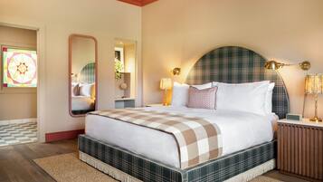 A neatly arranged bedroom with a large bed, a bedside table with a lamp, and a mirror on the wall.