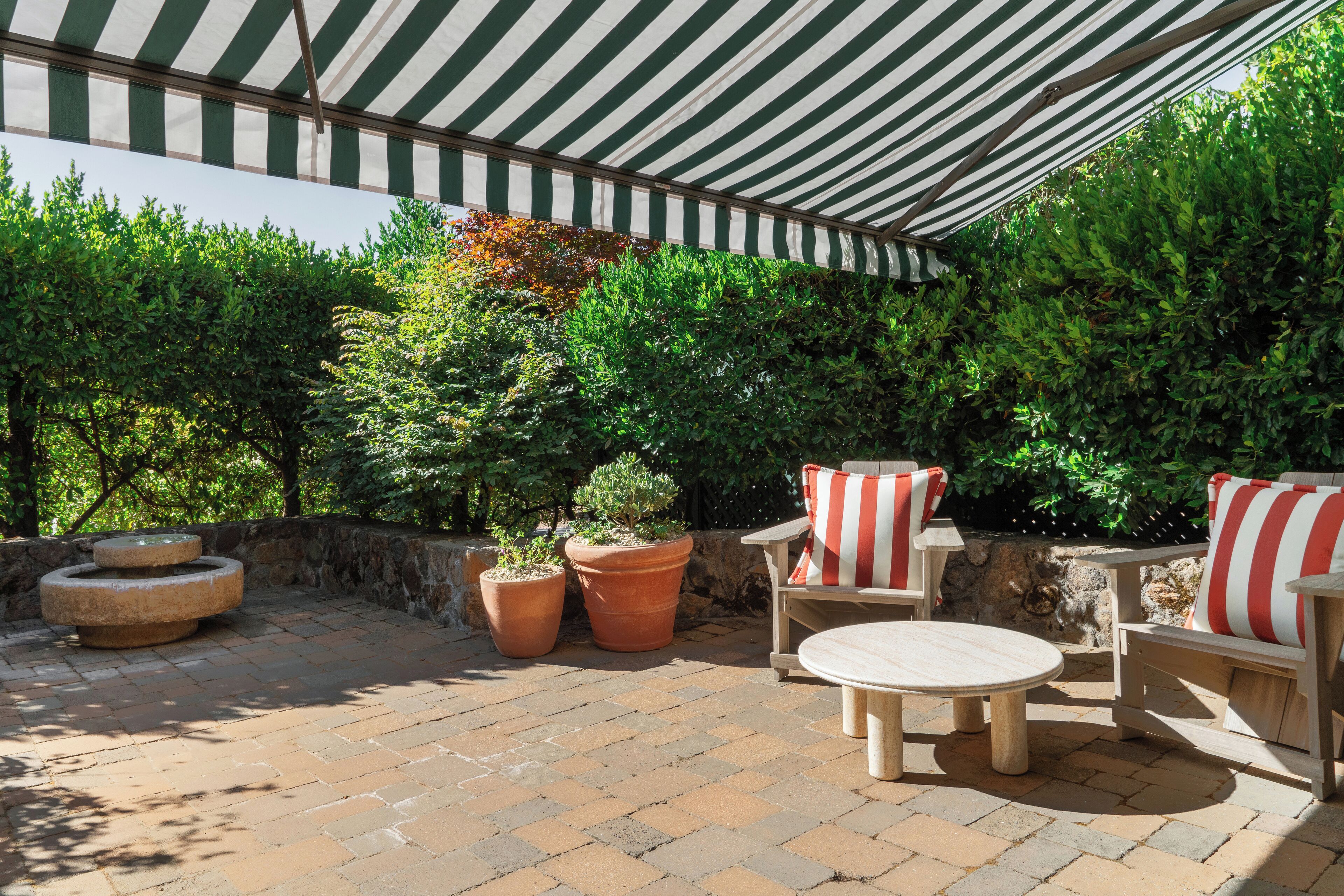 An outdoor patio area with a striped awning, terracotta planters, and wooden furniture.