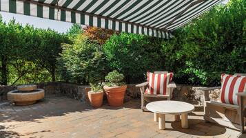 An outdoor patio area with a striped awning, terracotta planters, and wooden furniture.