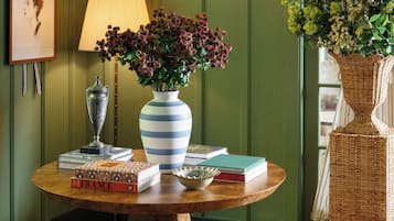 Una mesa redonda de madera con un jarrón de flores, libros y una lámpara.