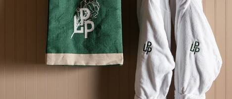 A bathroom with a wooden panel wall, a green and beige toiletry bag, and two white bathrobes with embroidered initials.