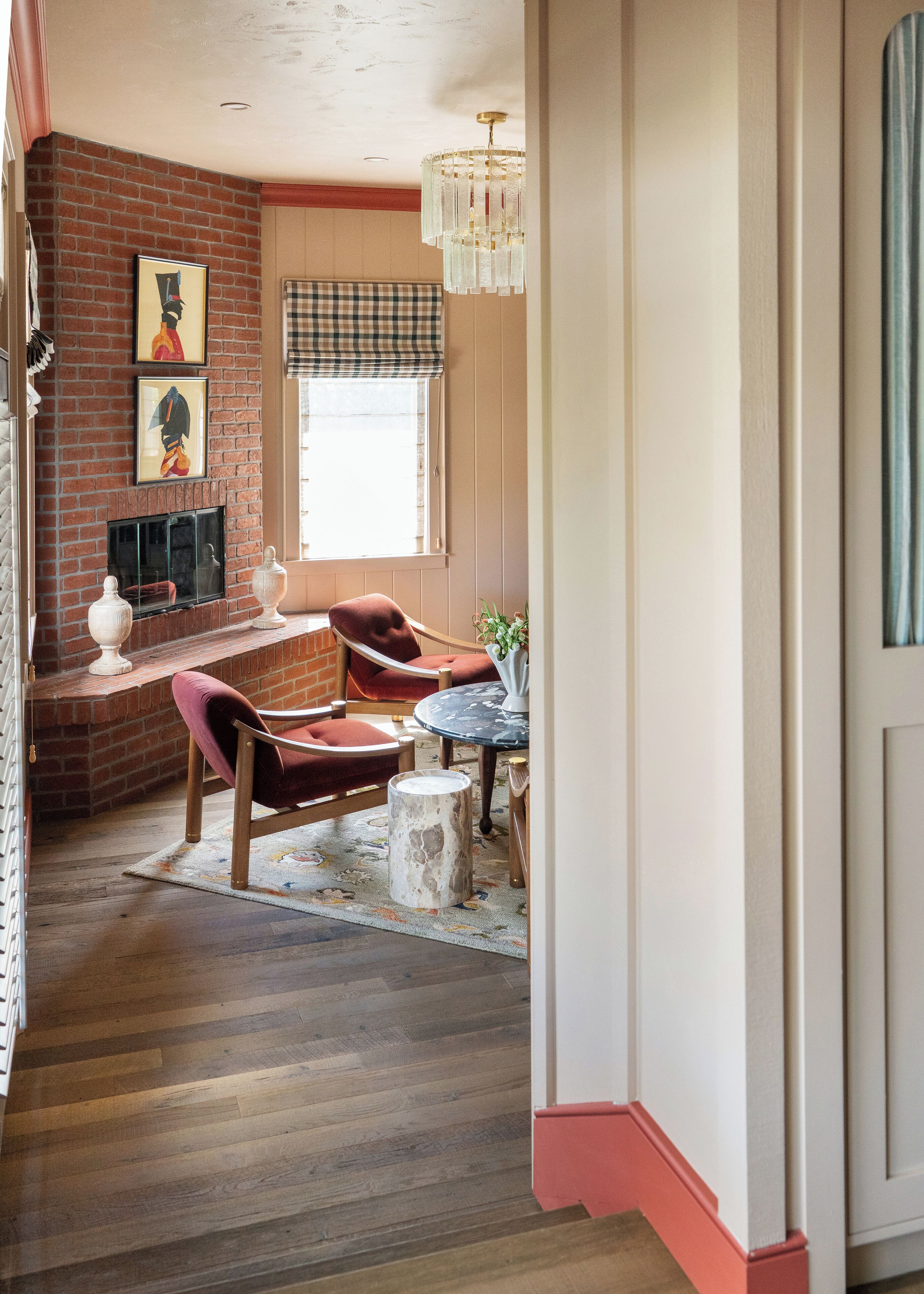 A cozy living room with a fireplace, a plaid window valance, and a chandelier.