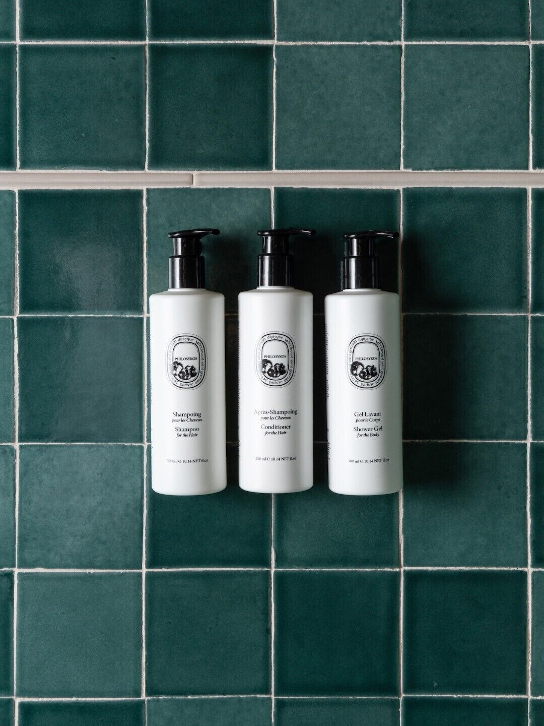 Three white bottles with black pumps against a green tiled background.