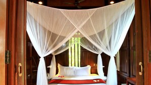 A wooden room with a bed under a white canopy, wooden floors, and a ceiling fan. - Sugar Hut 1984 (Pattaya)