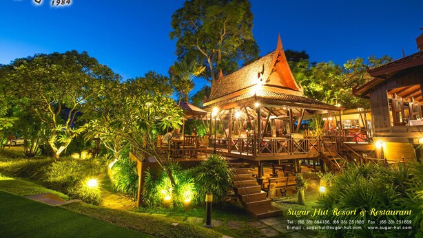 A resort with a traditional architectural style, featuring a prominent building with a tiled roof and a wooden deck. - Sugar Hut 1984 (Pattaya)