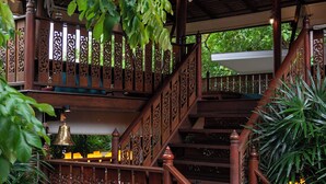 A wooden staircase with intricate railings and a bell hanging from the railing. - Sugar Hut 1984 (Pattaya)