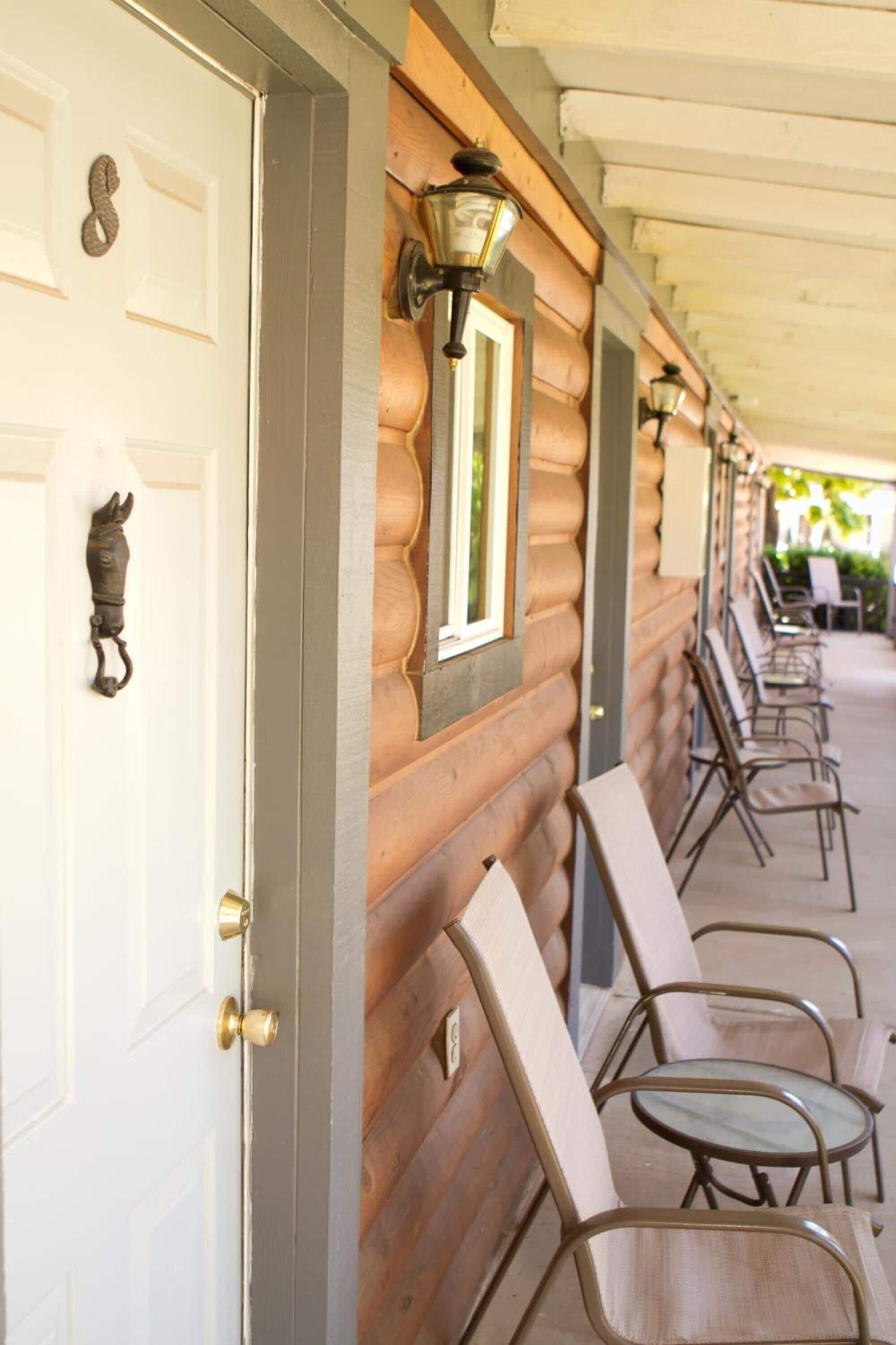 A wooden exterior wall with a row of metal chairs and a white door with a horse-shaped handle.