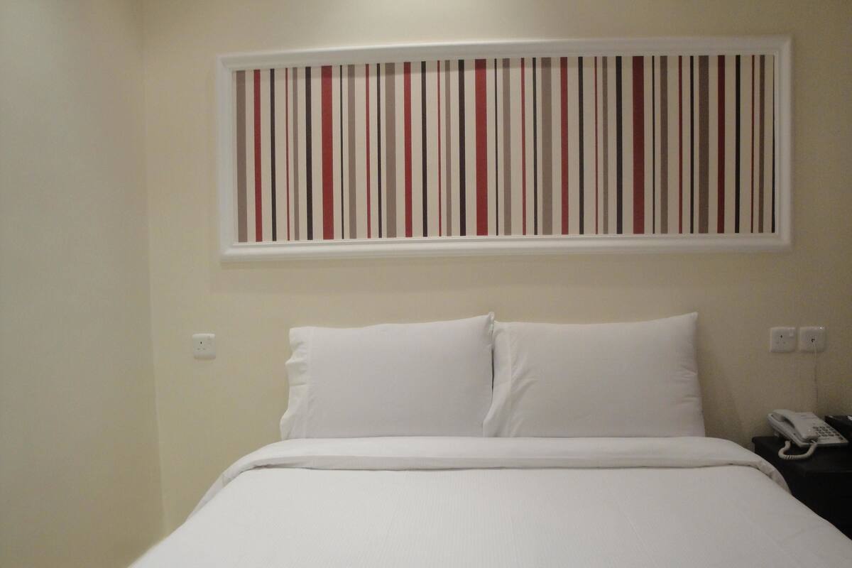 Ein ordentlich bezogenes Bett mit weißer Bettwäsche, einem an der Wand montierten Telefon und einer gestreiften Wanddekoration darüber.