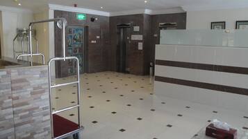 Un vestíbulo de hotel con piso de baldosas, un mostrador de recepción, un elevador empotrado en la pared y una señal de salida visible.