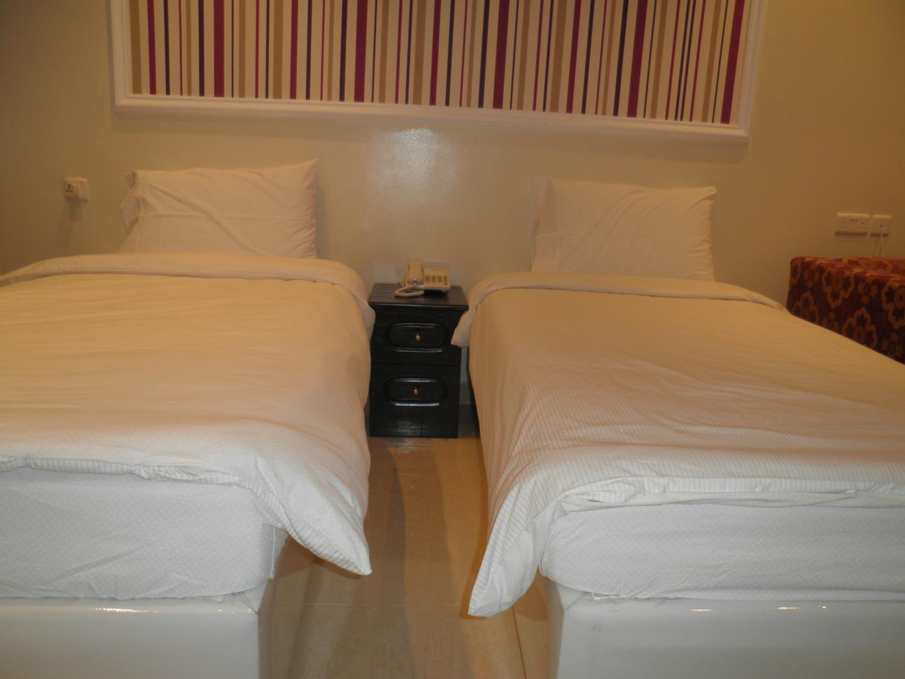 Een hotelkamer met twee enkele bedden, een nachtkastje met een telefoon, en een gestreept behang.