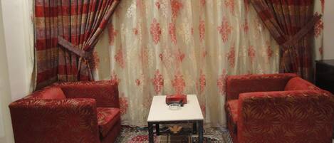 A room with two red upholstered sofas, a small white table with a glass object, and a patterned rug.