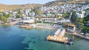 A coastal resort with clear waters, a dock with sun loungers, and a hillside of white buildings. - Avantgarde Refined Yalıkavak (Bodrum)