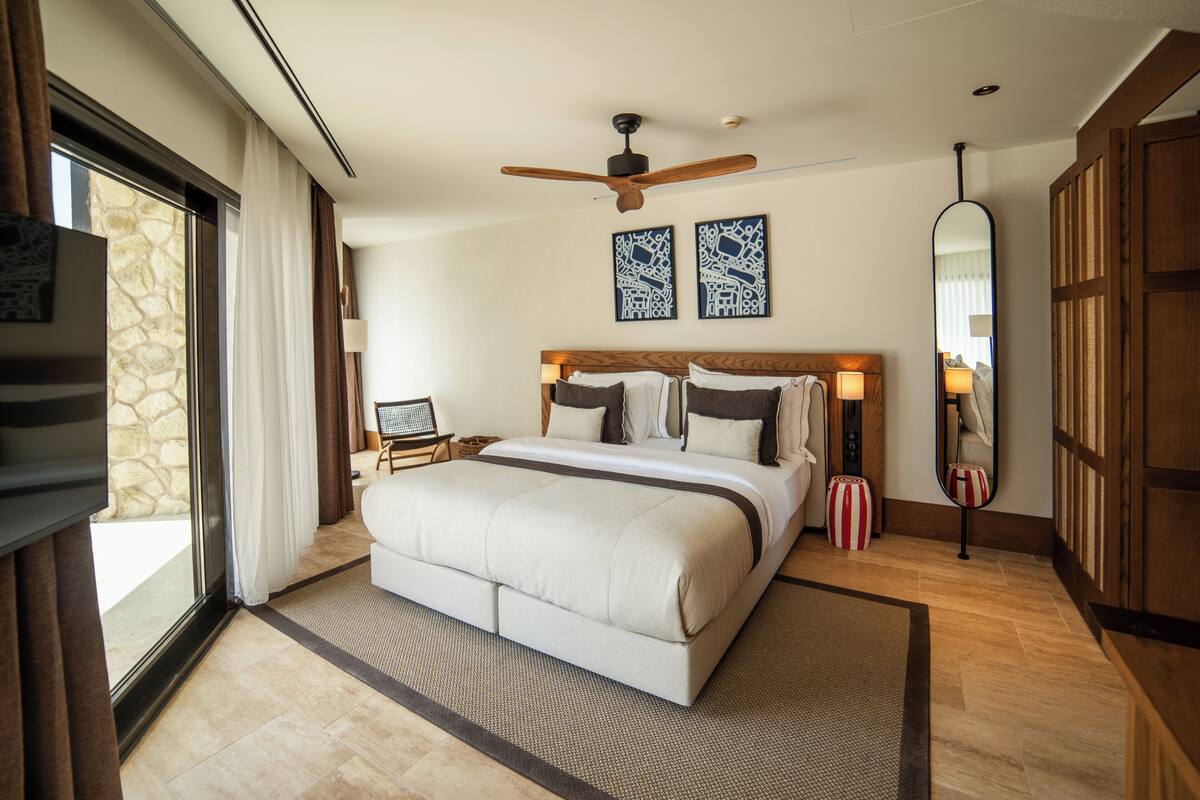 Um quarto espaçoso com uma cama grande, um ventilador de teto e vista para o exterior por uma porta de correr.